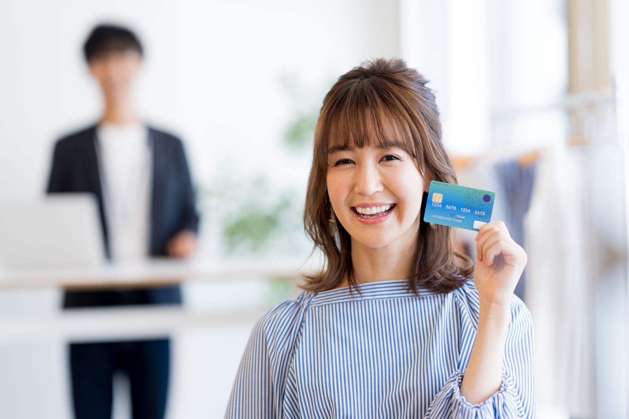 後ろでパソコンを操作する男性と手前でクレジットカードを持ち微笑む女性