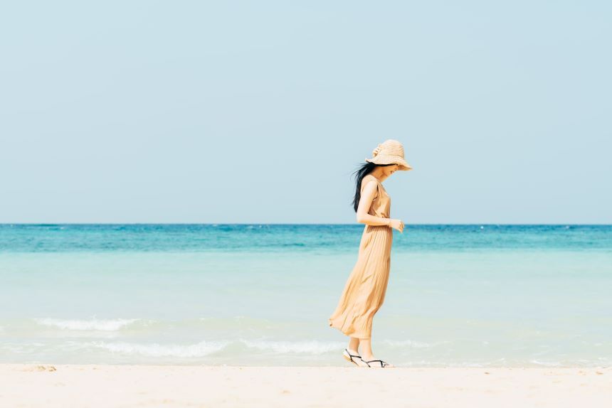 きれいな砂浜に立つワンピースと帽子を身に着けている女性