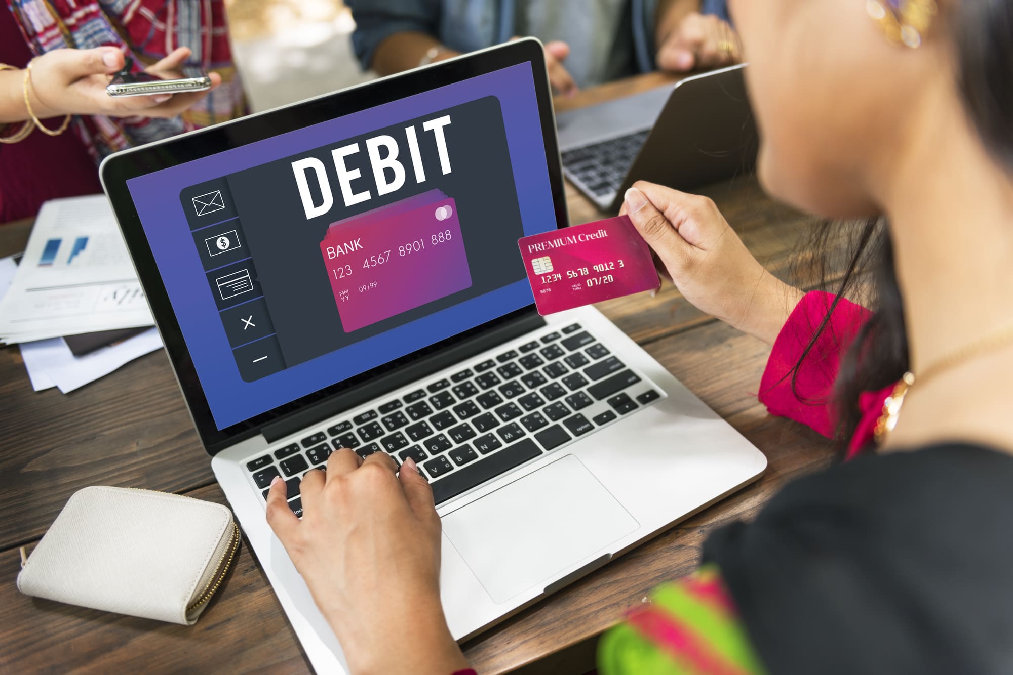 「DEBIT」が表示されたパソコン画面の前でデビッドカードを持つ女性