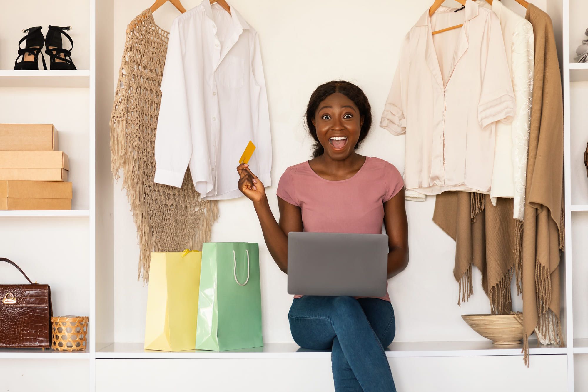 パソコンを見ながらクレジットカードを手に取り喜ぶピンクのシャツを着た女性